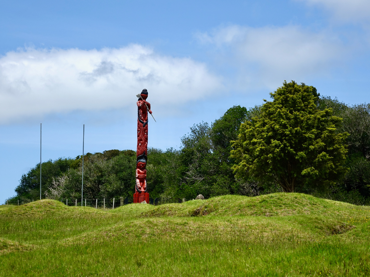 Ruapekapeka Pa, green rolling hills and a Maori pou whenua representing the fighting spirit and weapons used.